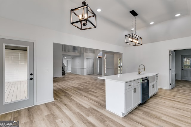 kitchen featuring white cabinets, sink, an island with sink, decorative light fixtures, and light hardwood / wood-style floors