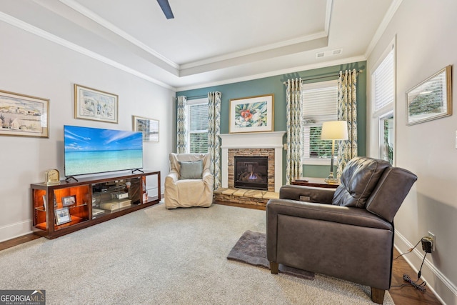 living room featuring ceiling fan, a stone fireplace, crown molding, and a tray ceiling