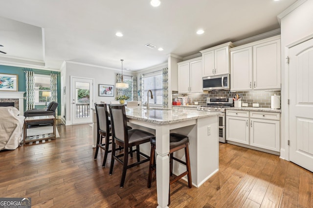 kitchen featuring appliances with stainless steel finishes, a center island with sink, white cabinetry, and decorative light fixtures