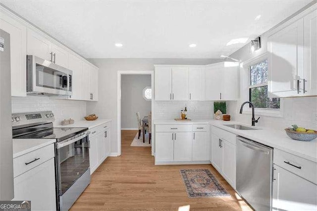 kitchen with backsplash, white cabinets, sink, light hardwood / wood-style flooring, and appliances with stainless steel finishes