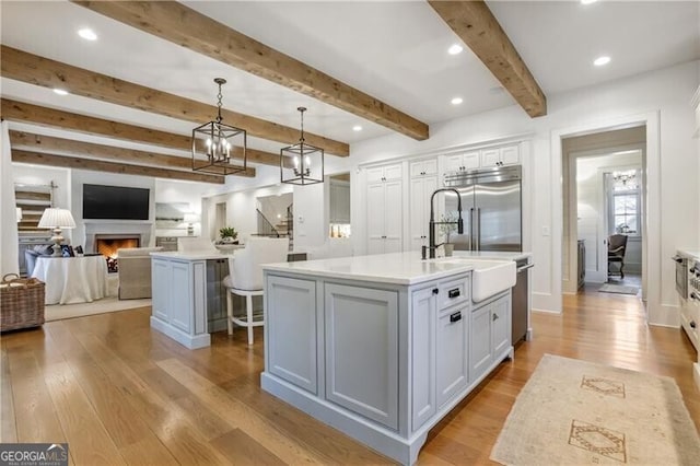 kitchen with stainless steel appliances, a kitchen island with sink, pendant lighting, white cabinets, and light hardwood / wood-style floors