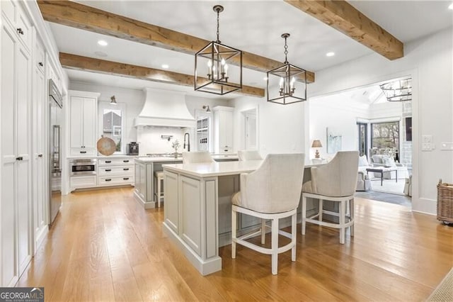 kitchen featuring custom exhaust hood, a breakfast bar, white cabinets, light hardwood / wood-style floors, and hanging light fixtures