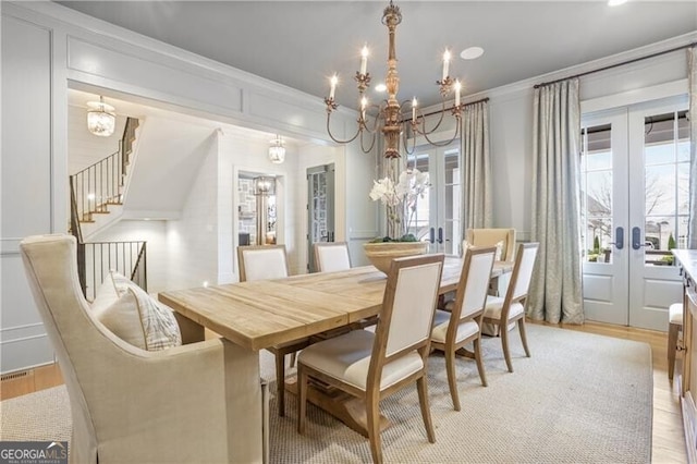 dining area with french doors, light wood-type flooring, an inviting chandelier, and ornamental molding