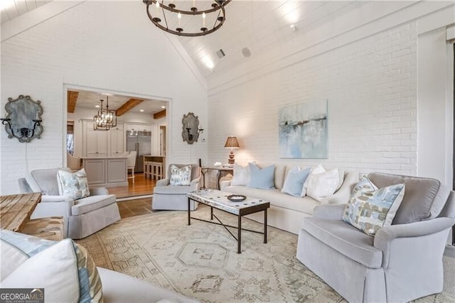 living room with a chandelier, high vaulted ceiling, beamed ceiling, and brick wall