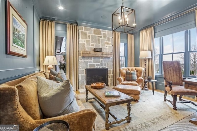 living area with a chandelier, a stone fireplace, and ornamental molding