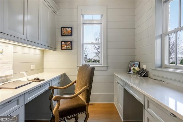 office with wood walls, plenty of natural light, light hardwood / wood-style floors, and built in desk