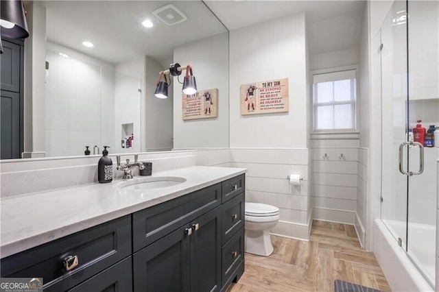 full bathroom featuring vanity, bath / shower combo with glass door, toilet, parquet flooring, and tile walls