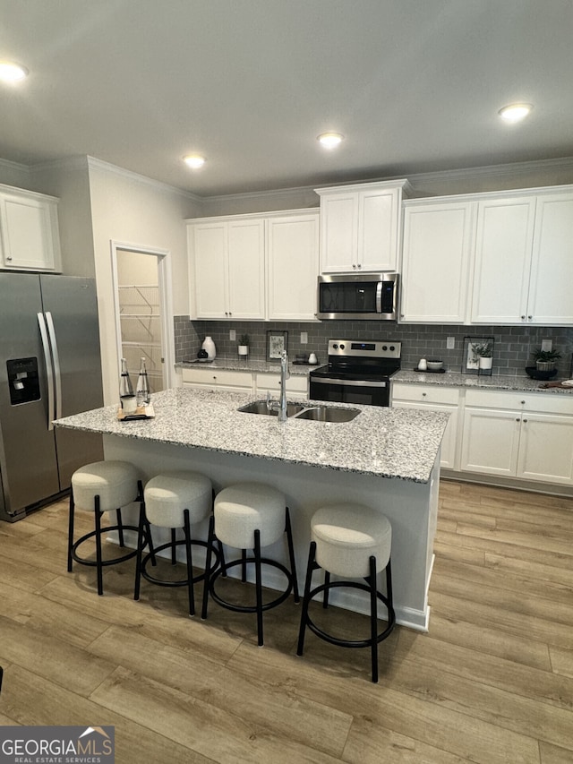 kitchen featuring white cabinetry, stainless steel appliances, a breakfast bar, and a center island with sink