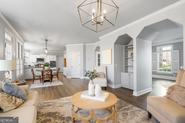 living room featuring a tiled fireplace, dark wood-type flooring, a notable chandelier, and ornamental molding