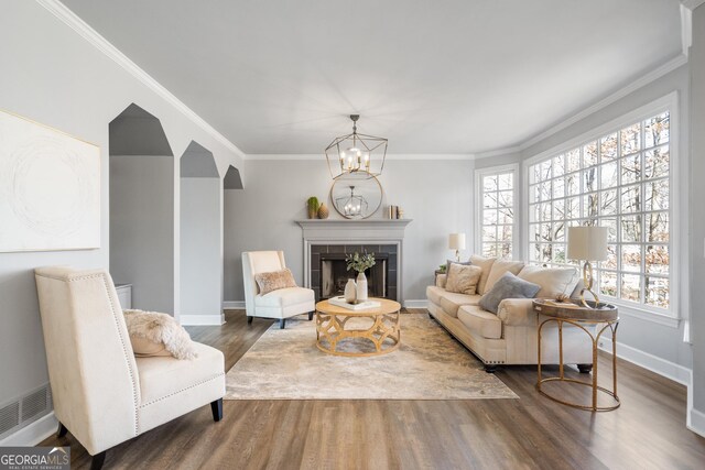 living room featuring a tile fireplace, an inviting chandelier, ornamental molding, and dark hardwood / wood-style flooring