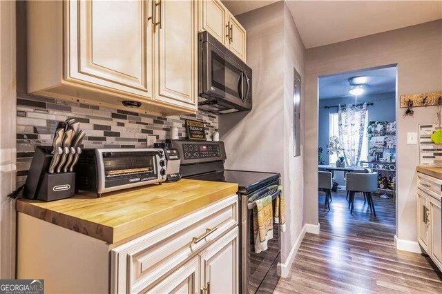 kitchen with electric range, tasteful backsplash, dark hardwood / wood-style flooring, butcher block countertops, and cream cabinets