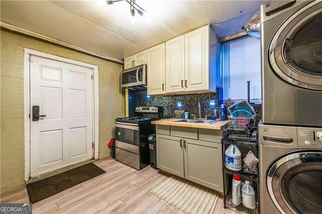 kitchen with butcher block counters, sink, stainless steel appliances, stacked washer and dryer, and light hardwood / wood-style floors