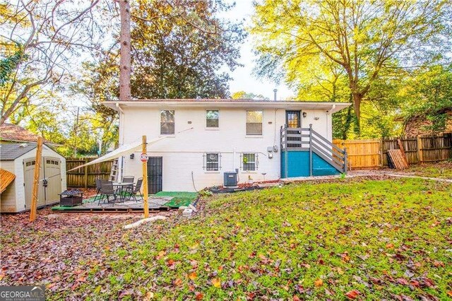 rear view of house with a lawn, a wooden deck, cooling unit, and a storage unit