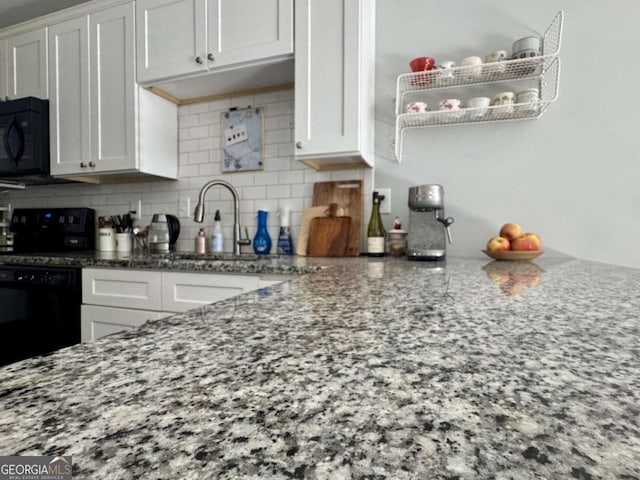 kitchen with white cabinets, black appliances, sink, light stone countertops, and tasteful backsplash