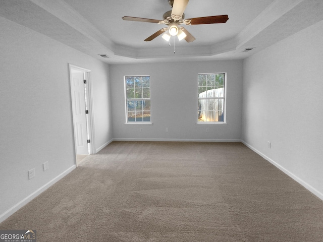 empty room featuring a raised ceiling, ceiling fan, and light colored carpet