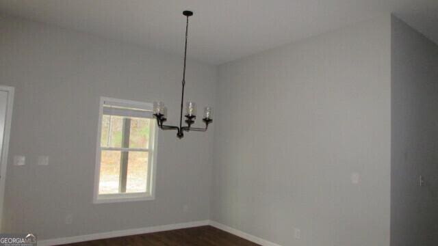 unfurnished dining area featuring dark wood-type flooring and an inviting chandelier