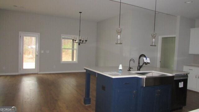 kitchen with dark hardwood / wood-style flooring, blue cabinetry, pendant lighting, a center island with sink, and white cabinets