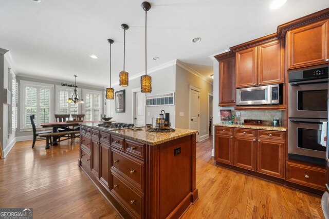 kitchen featuring a center island, hanging light fixtures, light stone counters, crown molding, and appliances with stainless steel finishes