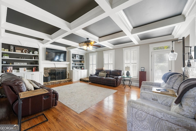 living room with ceiling fan, coffered ceiling, built in features, light hardwood / wood-style floors, and a fireplace