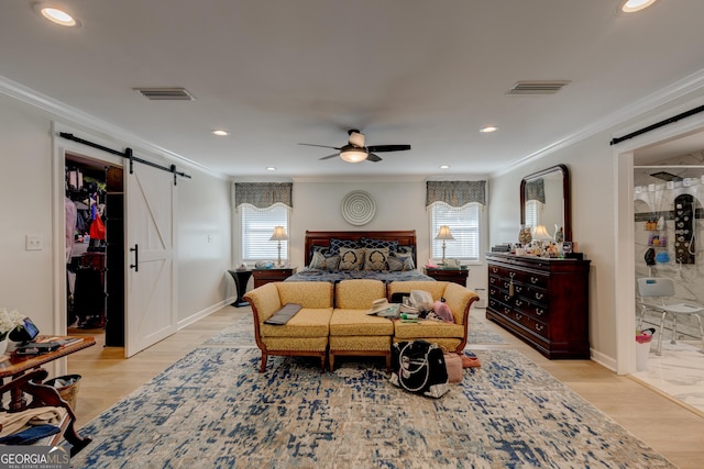 bedroom featuring ceiling fan, a barn door, light hardwood / wood-style flooring, ensuite bathroom, and ornamental molding