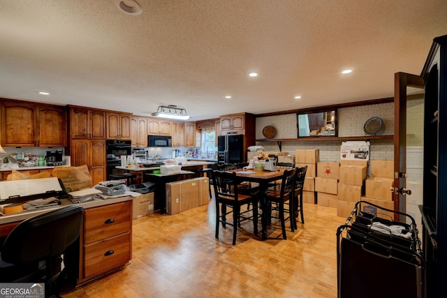 kitchen featuring brick wall, light hardwood / wood-style floors, a textured ceiling, a kitchen bar, and black appliances