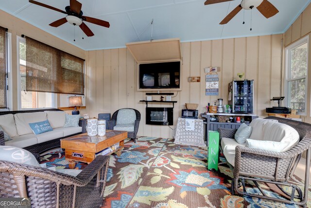 living room with wooden walls, ceiling fan, and a healthy amount of sunlight