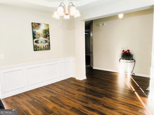 empty room with dark hardwood / wood-style floors and a notable chandelier