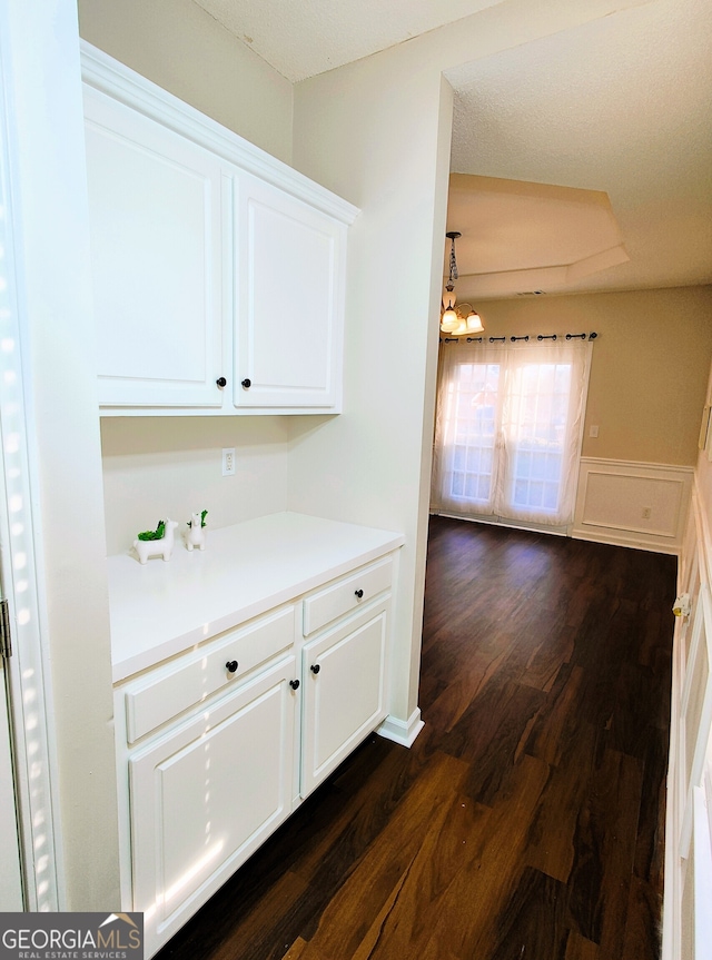 bar with a chandelier, white cabinets, and dark wood-type flooring