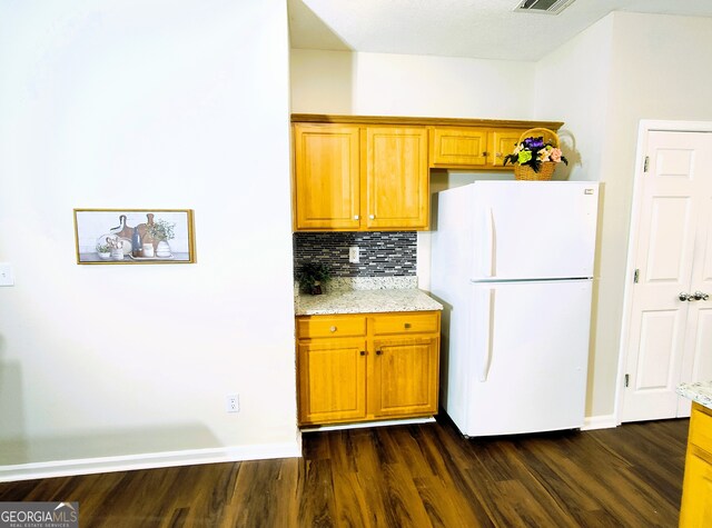 kitchen featuring decorative backsplash, white refrigerator, light stone counters, and dark hardwood / wood-style floors