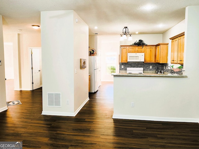 kitchen with light stone counters, dark hardwood / wood-style flooring, kitchen peninsula, white appliances, and decorative backsplash