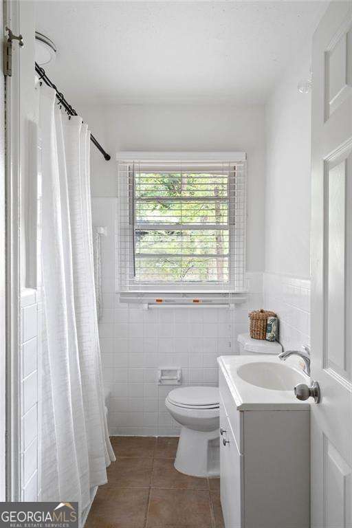 bathroom featuring toilet, vanity, tile patterned floors, and tile walls