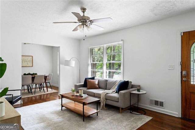 living room with a textured ceiling, ceiling fan, and dark wood-type flooring