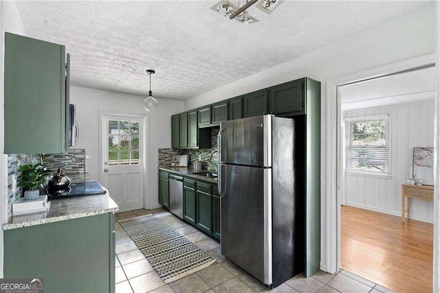 kitchen with backsplash, light tile patterned flooring, stainless steel appliances, and green cabinetry