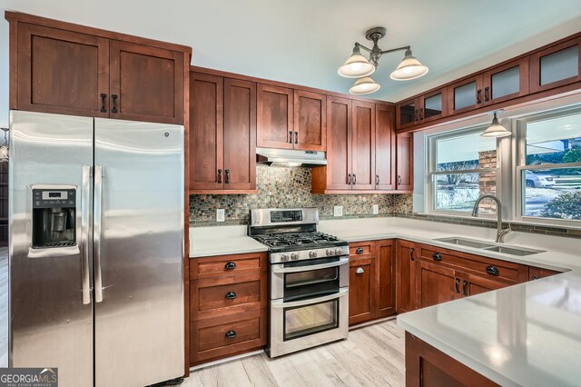 kitchen featuring sink, stainless steel appliances, light hardwood / wood-style flooring, backsplash, and pendant lighting