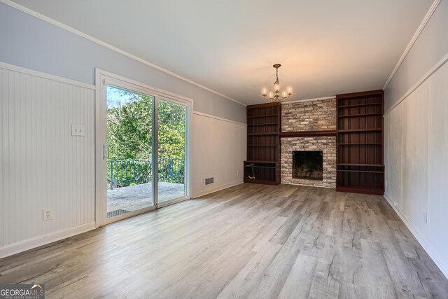 unfurnished living room with built in features, ornamental molding, a notable chandelier, and a brick fireplace