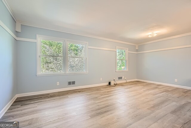 empty room with light hardwood / wood-style floors, a wealth of natural light, and crown molding