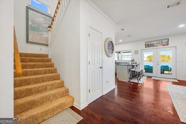 stairway with french doors, ornamental molding, a healthy amount of sunlight, and hardwood / wood-style floors