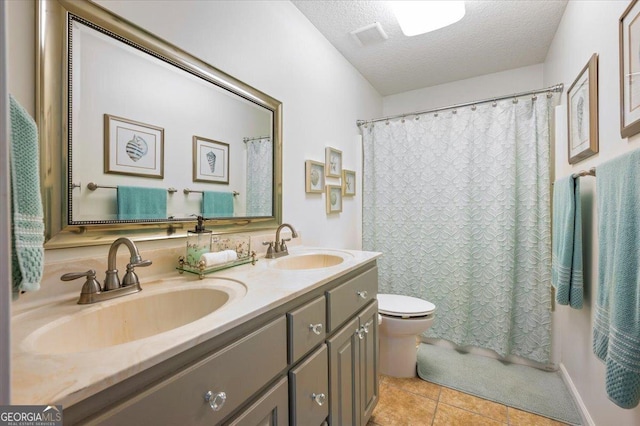 bathroom featuring tile patterned floors, toilet, a sink, a textured ceiling, and double vanity