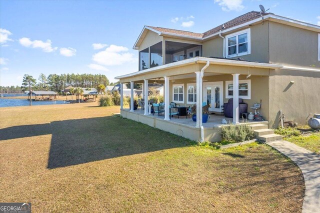 rear view of property featuring french doors, a water view, a sunroom, a yard, and a patio