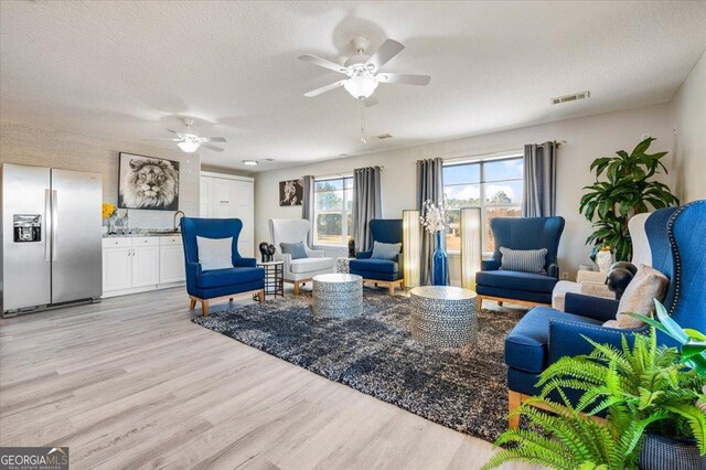 living room featuring ceiling fan, a textured ceiling, and light hardwood / wood-style flooring