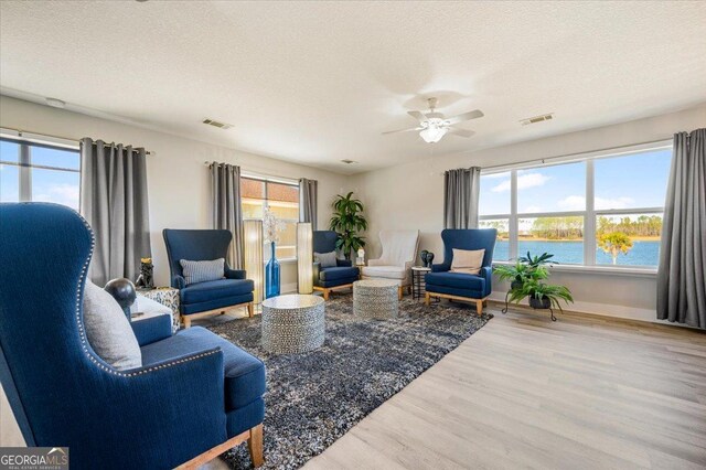 living room with a textured ceiling, a water view, hardwood / wood-style flooring, and a healthy amount of sunlight