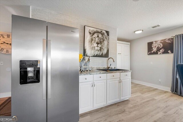 kitchen with white cabinets, sink, stainless steel refrigerator with ice dispenser, light wood-type flooring, and a textured ceiling