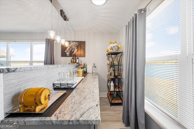 kitchen featuring a water view, light stone countertops, hanging light fixtures, and light hardwood / wood-style flooring