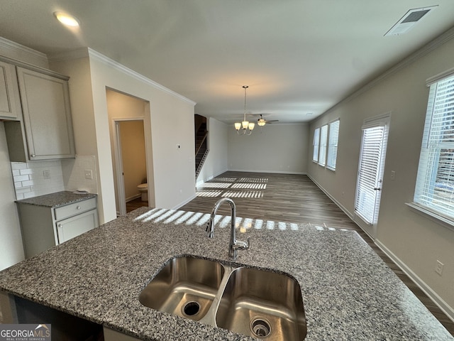 kitchen with gray cabinetry, stone counters, sink, crown molding, and decorative backsplash