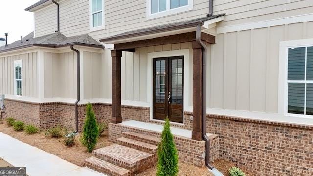 view of exterior entry with french doors, brick siding, and board and batten siding