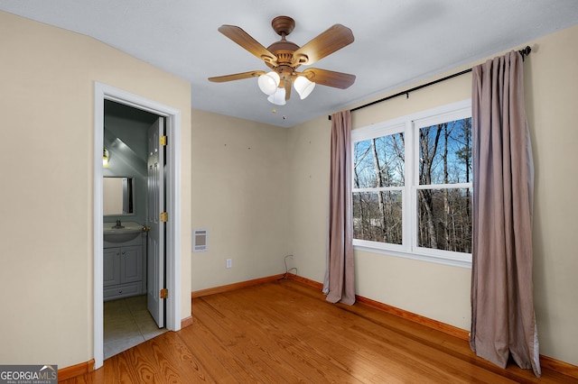 unfurnished bedroom featuring ensuite bathroom, heating unit, ceiling fan, sink, and light hardwood / wood-style flooring