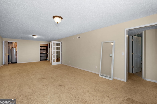 spare room featuring a textured ceiling, electric water heater, and light colored carpet