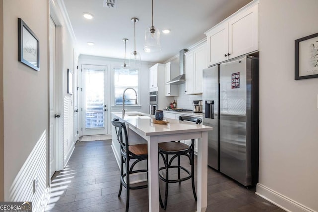 kitchen featuring white cabinetry, wall chimney exhaust hood, decorative light fixtures, a kitchen bar, and appliances with stainless steel finishes