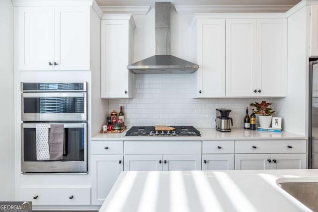 kitchen featuring white cabinetry, wall chimney range hood, appliances with stainless steel finishes, and tasteful backsplash