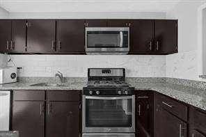 kitchen with light stone countertops, dark brown cabinets, stainless steel appliances, and sink